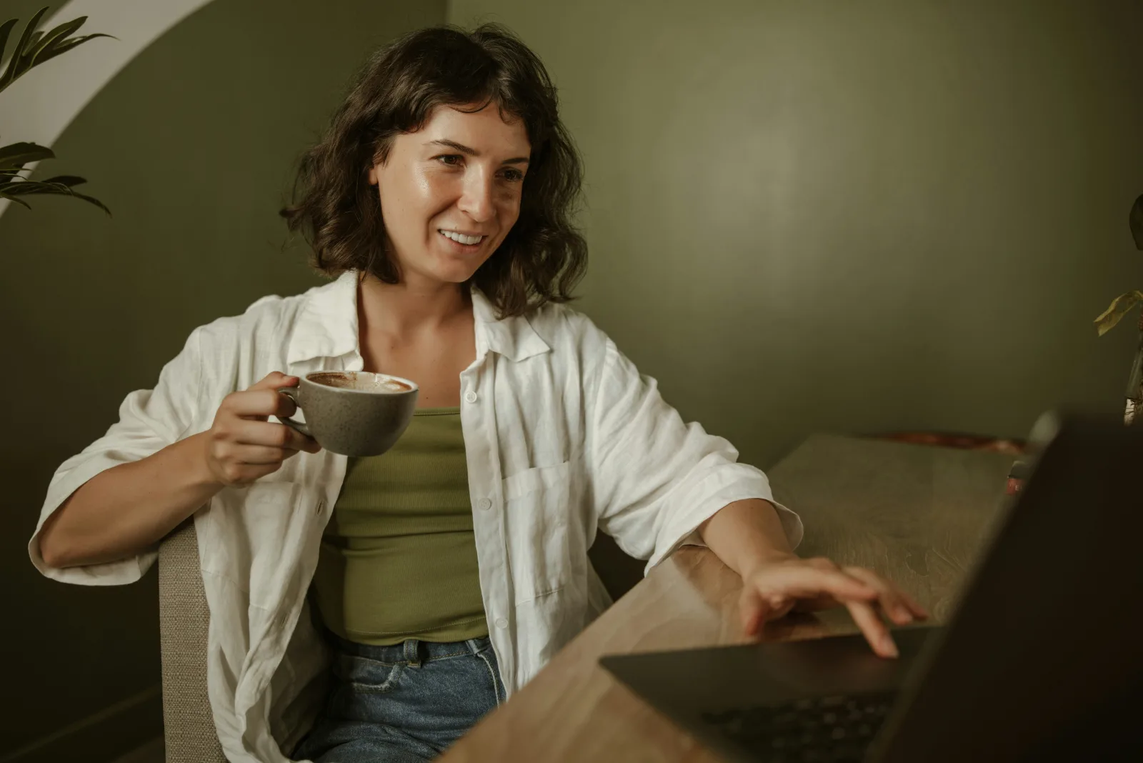 Eine Frau mit Kaffeetasse lächelt an ihrem Laptop – mitten in einer Online-Session