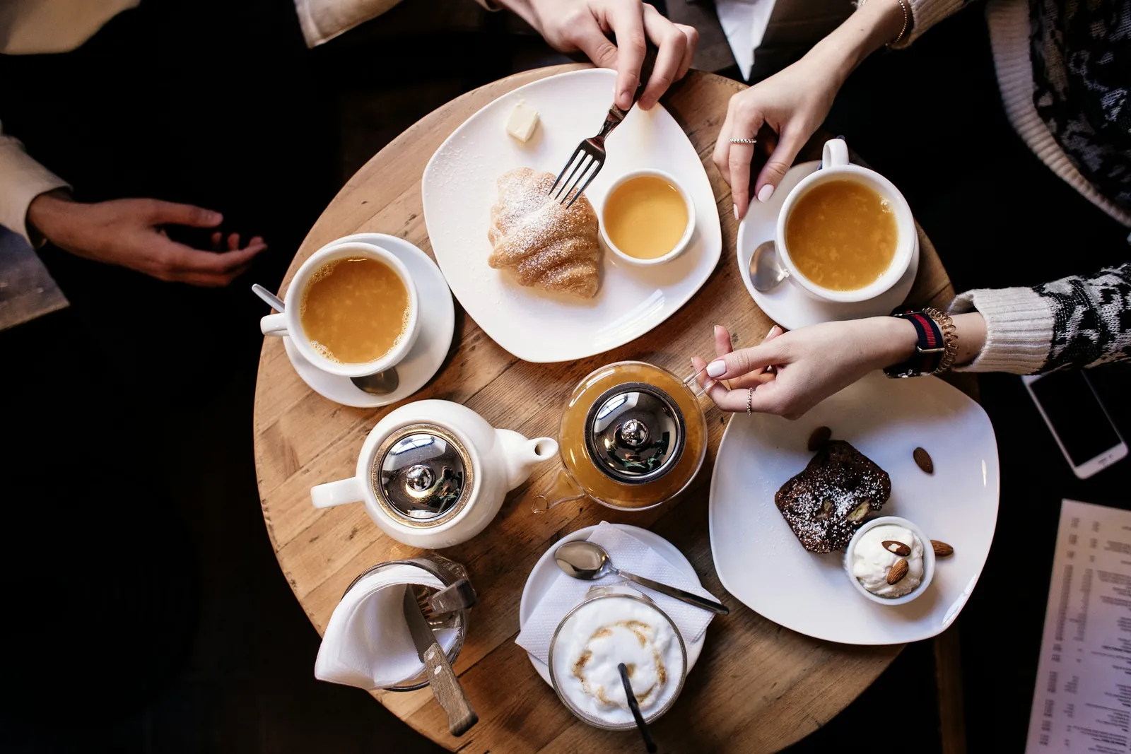 Mehrere Hände an einem runden Tisch mit Tee, Kaffee und Kuchen