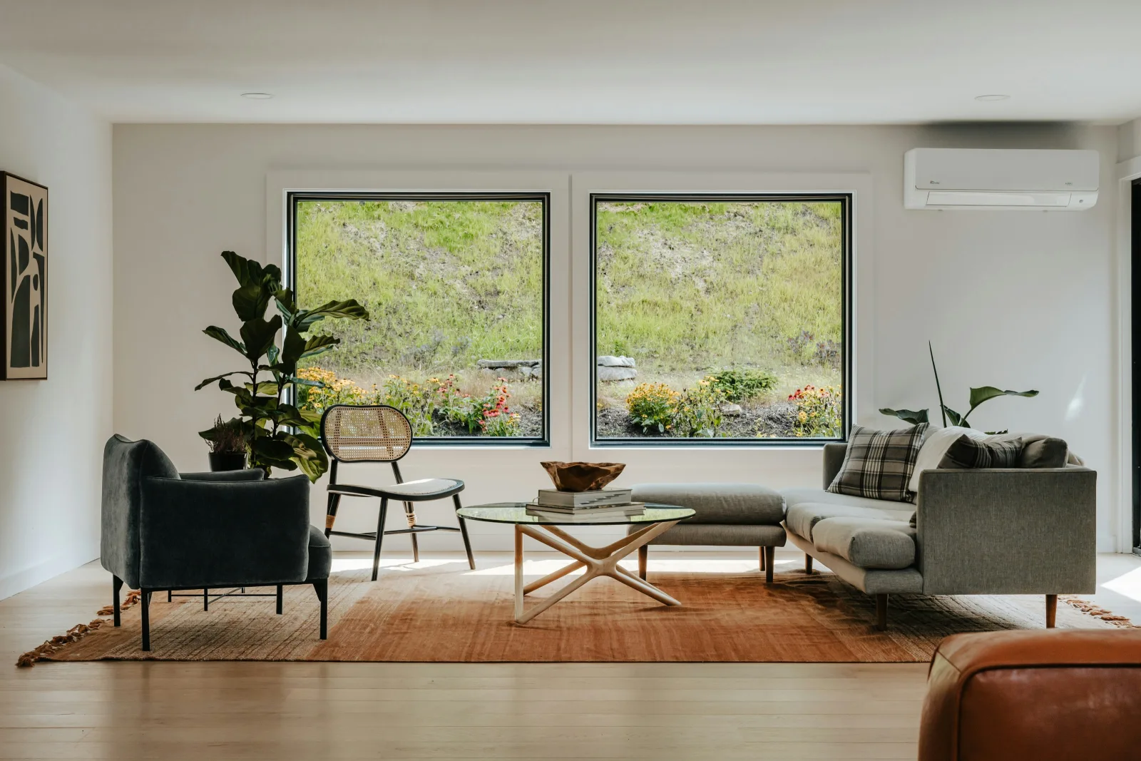 Ein heller Raum mit Sofa, Sessel und Stuhl um einen Couchtisch, große Fenster ins Grüne