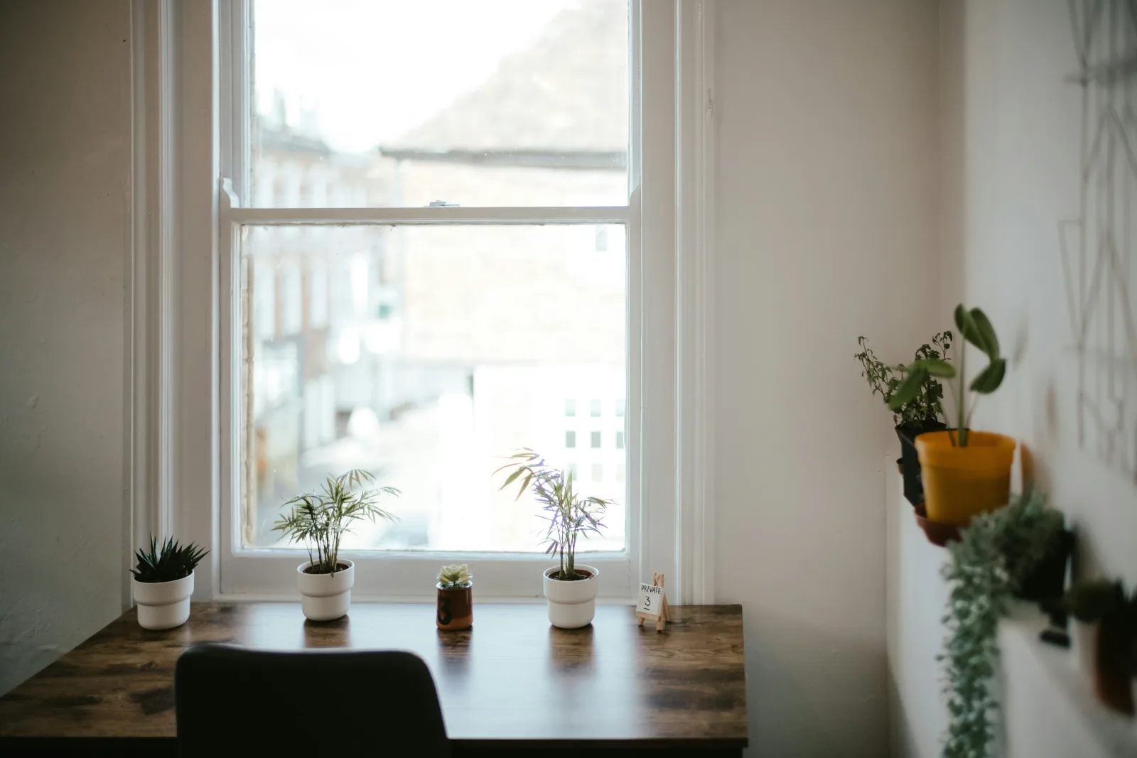 Ein Schreibtisch mit Stuhl vor einem Fenster, Pflanzen auf der Fensterbank